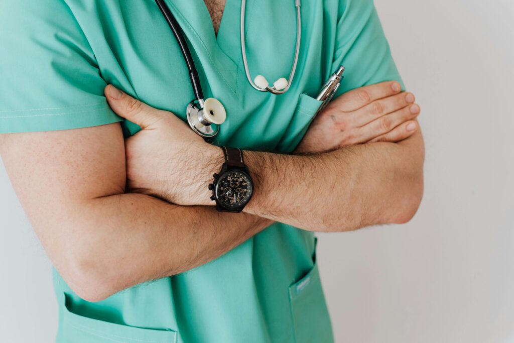 Close-up of a male doctor in scrubs with crossed arms and stethoscope on white background.